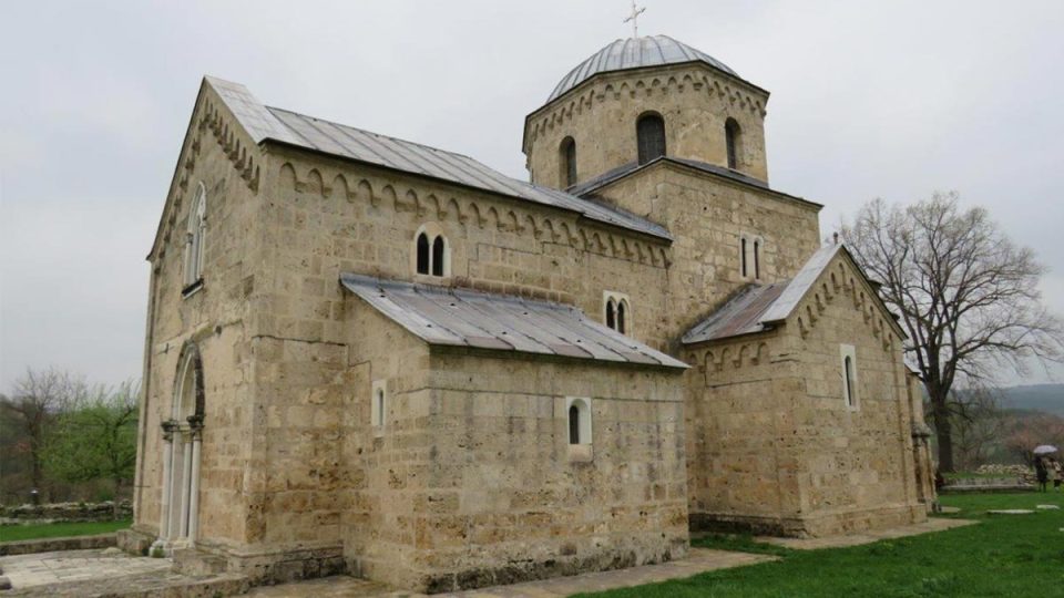 Kamena crkva manastira Gradac sa kupolom i metalnim krovom, na travnatoj porti pod oblačnim nebom.