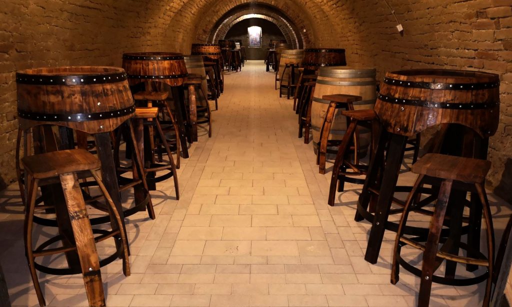 odrum vinarije sa svodovima od cigle i stolovima od drvenih buradi, poređanim duž hodnika.